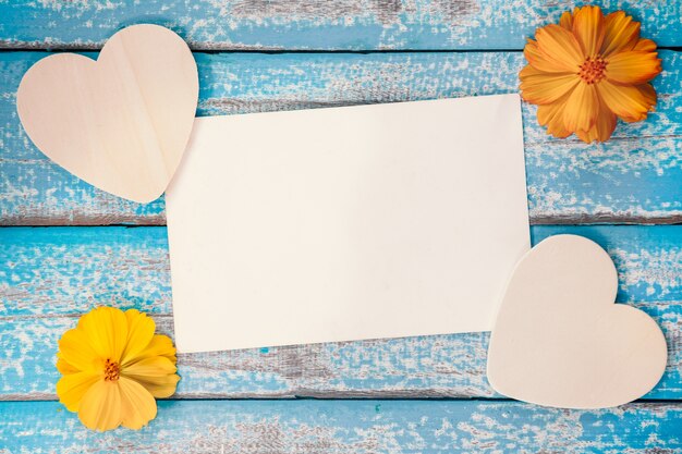 El álbum en blanco del marco de la foto adorna con forma de la flor y del corazón en viejo fondo de madera azul