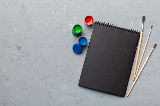 Albumseiten und Farben Bleistiftpinsel auf farbigem Hintergrund Draufsicht mit leerem Raum Arbeitsplatz für Kreativität Konzeptzeichnung für den Heimunterricht