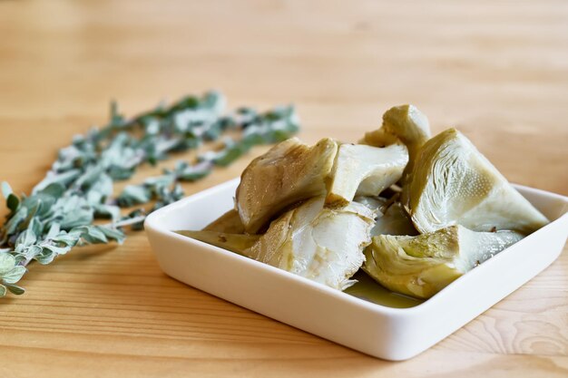 Alcachofa en escabeche con ajo en plato blanco sobre mesa de madera