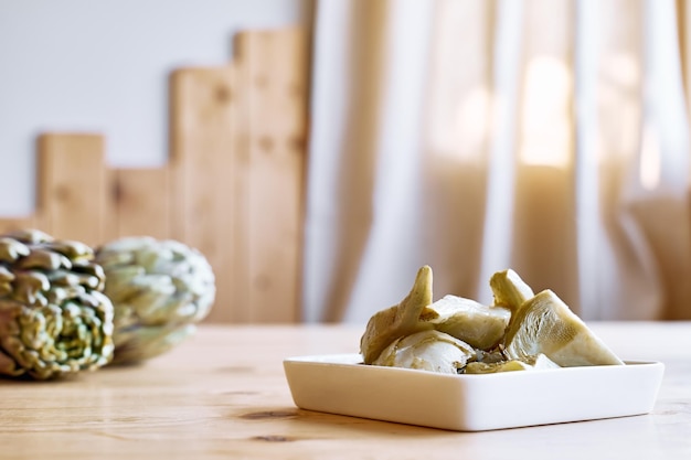 Alcachofa en escabeche con ajo en plato blanco sobre mesa de madera