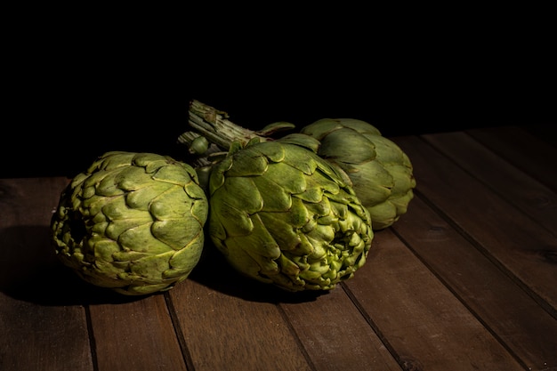 Foto alcachofas en mesa de madera con fondo negro.