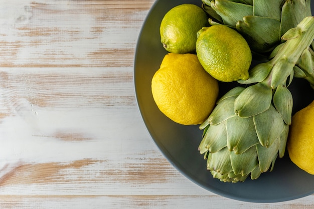 Alcachofras orgânicas maduras em uma mesa de madeira branca com limão.