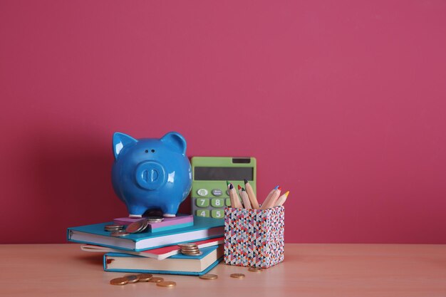 Foto alcancía con libros, monedas, calculadora y lápices de colores sobre fondo de color