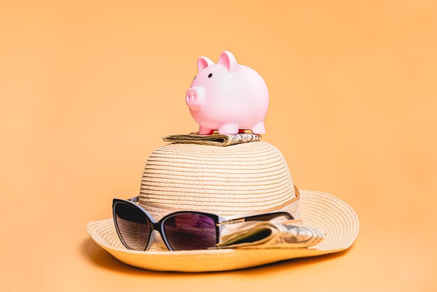 Una alcancía sobre un sombrero para el sol de mujer sobre un fondo naranja Gafas de sol y billetes de dólar