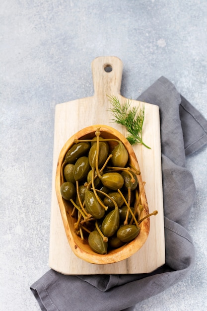 Alcaparras enlatadas en plato de madera, tapenade y pan sobre fondo de hormigón de moda. Vista superior