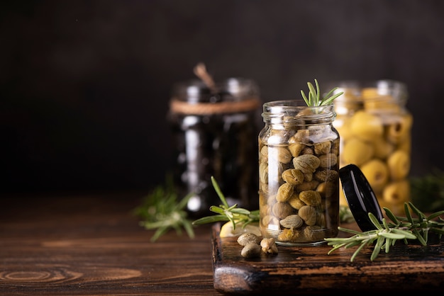 Alcaparras en escabeche en un frasco de vidrio con hierbas sobre mesa de madera