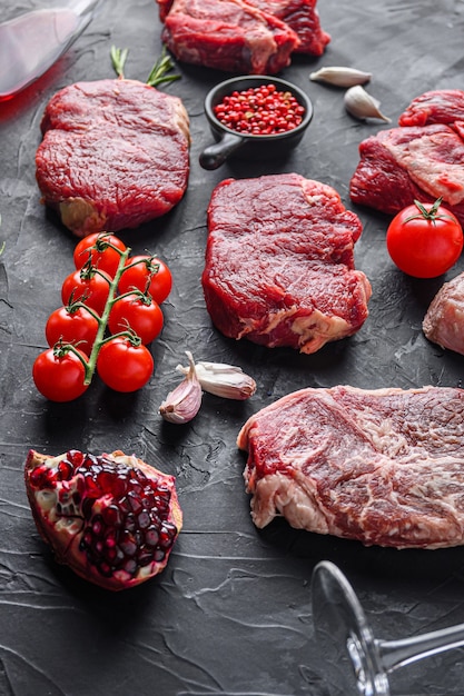 Alcatra, cortes de bife de carne, na frente do bife de lâmina superior com ervas, temperos e copo de vinho tinto na mesa preta, vista lateral.