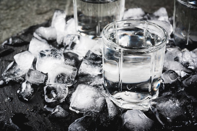 Alcohol y cócteles. Tres vasos de vodka en una bandeja de pizarra, con hielo. Sobre una mesa de piedra negra, vista superior