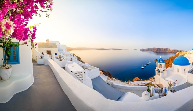 Aldeia grega tradicional de Oia de Santorini, com cúpulas azuis contra o mar Aegan e caldeira com flores