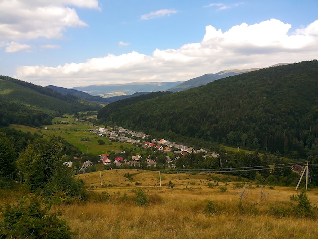 Aldeia no vale tendo como pano de fundo várias montanhas arborizadas e céu azul com nuvens