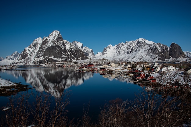 Aldeias e montanhas cobertas de neve com reflexo na água em um dia de céu azul claro