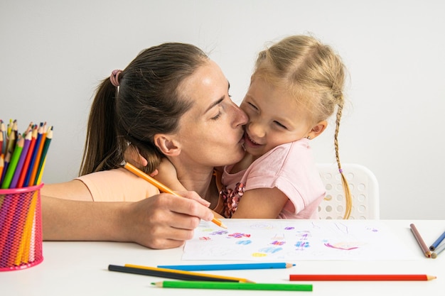 Alegre abrazando a mamá y niña dibujar juntos con lápices de colores sobre papel