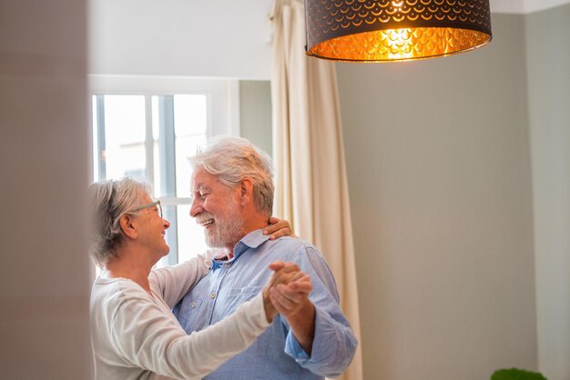 Foto alegre activa vieja pareja romántica jubilada bailando riendo en la sala de estar feliz esposa de mediana edad y marido mayor divirtiéndose en casa sonriendo abuelos ancianos de la familia relajándose uniéndose xa