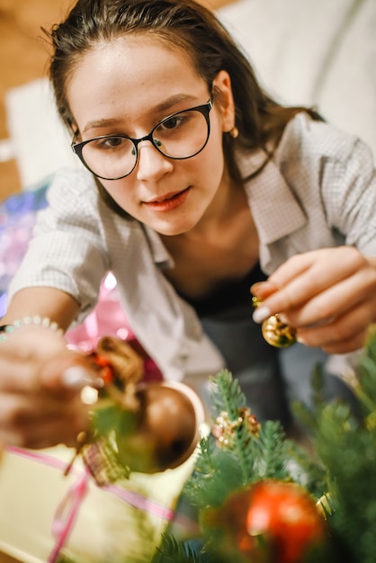 Alegre adolescente con gafas decora el árbol de Navidad