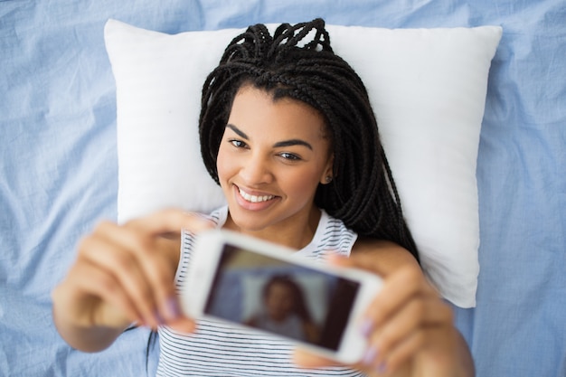 Alegre adolescente que toma selfie que miente en cama