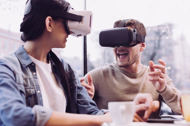 Alegre alegre pareja gay con gafas VR mientras el hombre gesticula y abre la boca