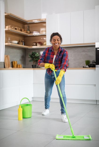 Alegre ama de casa afroamericana milenaria en guantes de goma con trapeador lava el piso