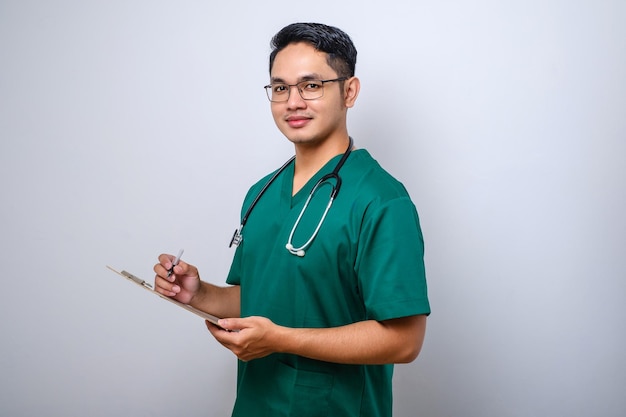 Alegre y amable médico asiático masculino con portapapeles durante el chequeo diario