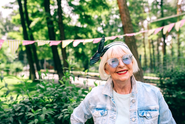 Alegre anciana elegante con cabello gris y gafas azules y maestro de vacaciones de mezclilla