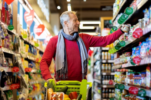 Alegre anciano eligiendo salsa en el supermercado