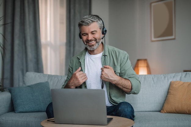 Alegre anciano europeo con barba en los auriculares se ha reunido de forma remota con el cliente en la computadora