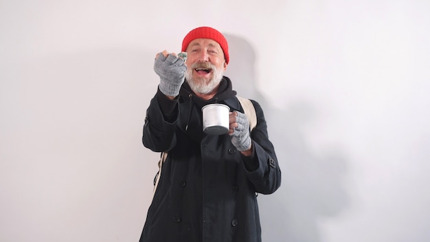 Alegre anciano sin hogar con barba en un sombrero sonrió con dinero en su mano sobre un fondo aislado