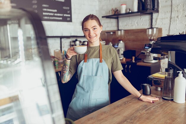 Foto alegre barista femenina con taza de café trabajando en café