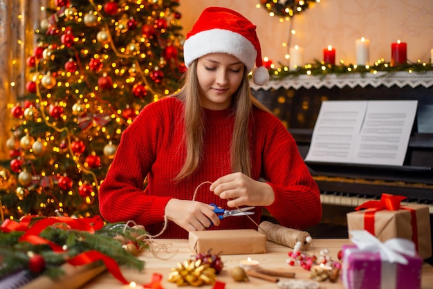 Alegre bastante joven envolviendo el regalo de Navidad Felices vacaciones en casa