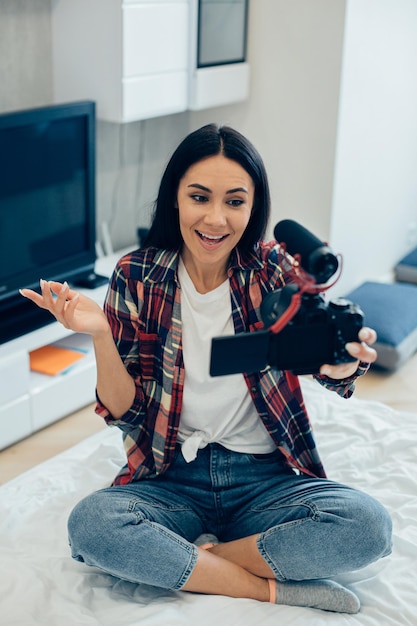 Foto alegre bloguera popular sonriendo y haciendo un nuevo video para sus seguidores mientras está sentada en la cama