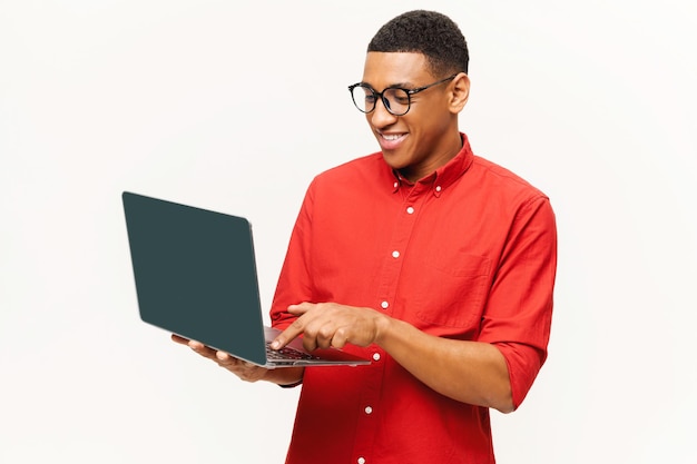 Alegre, bonito, sorridente, jovem afro-americano de camisa vermelha usando laptop isolado em branco.