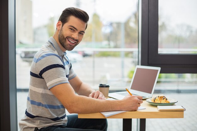 Alegre buen hombre positivo volviéndose hacia usted y sonriendo mientras toma notas