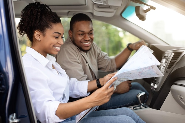 Alegre casal americano africano sentado no carro segurando o mapa turístico