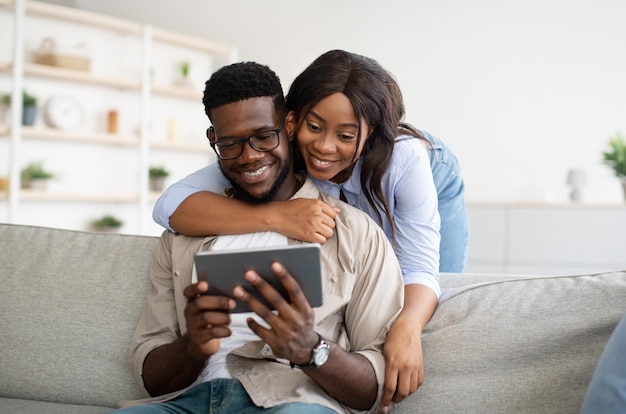 Alegre casal americano africano sentado no sofá usando tablet