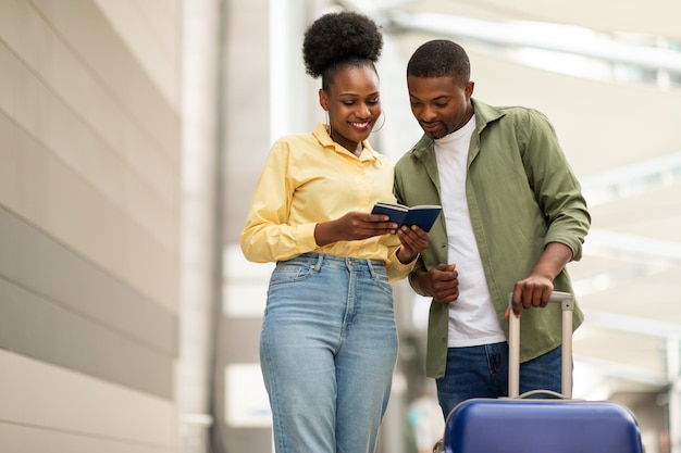 Alegre casal de turistas afro-americanos viajando juntos segurando passaportes ao ar livre