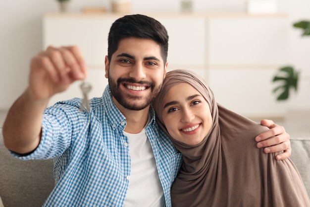 Alegre casal do Oriente Médio mostrando chave sorrindo sentado em casa