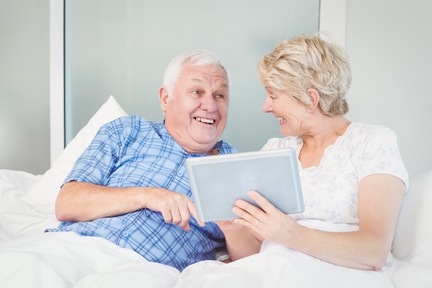 Alegre casal sênior usando mesa digital na cama