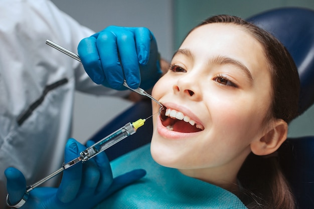 Alegre chica agradable sentarse en la silla dental y mantener la boca abierta