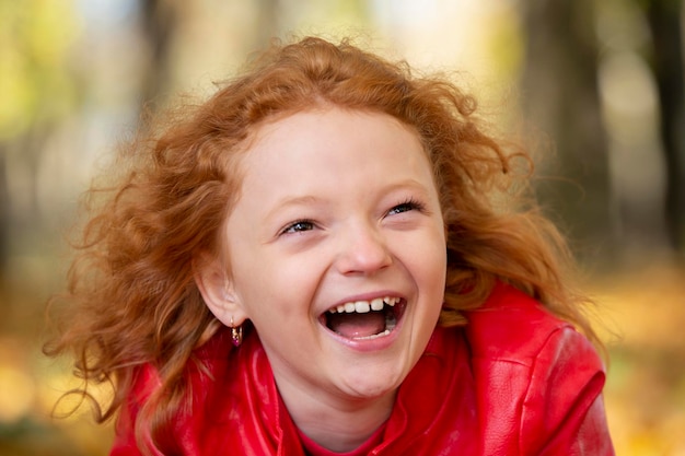 Alegre chica pelirroja riendo alegremente contra el telón de fondo de un parque de otoño