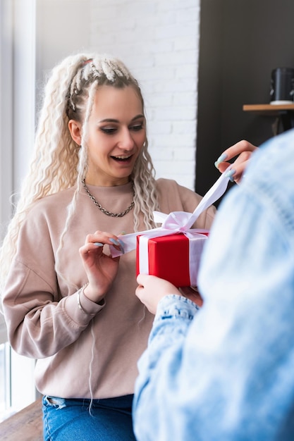 Foto alegre chica sorprendida abre un regalo el chico le da un regalo a la chica joven pareja alegre en ropa casual