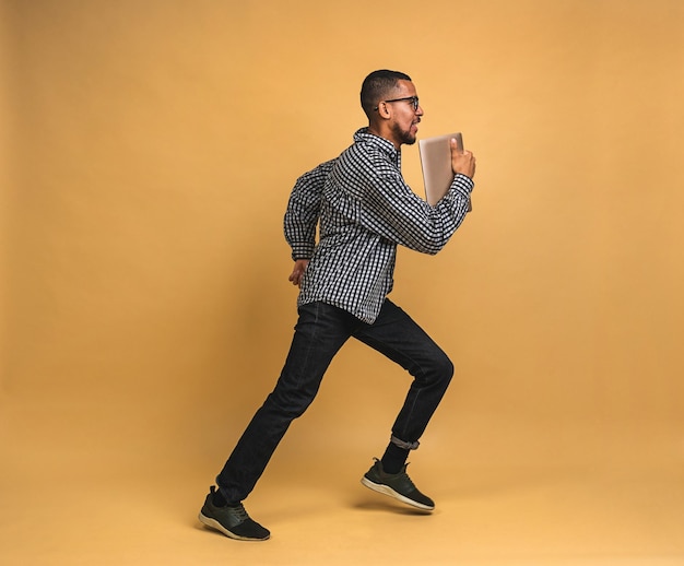 Alegre chico afroamericano saltando o bailando aislado sobre fondo beige Foto interior de un impresionante modelo masculino divirtiéndose en el estudio usando una computadora portátil