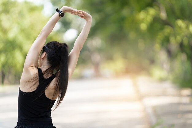 Una alegre corredora asiática en ropa deportiva haciendo estiramientos antes de hacer ejercicio al aire libre en el parque natural de la ciudad bajo el atardecer