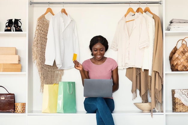 Alegre dama africana adicta a las compras comprando en línea a través de una computadora portátil en casa