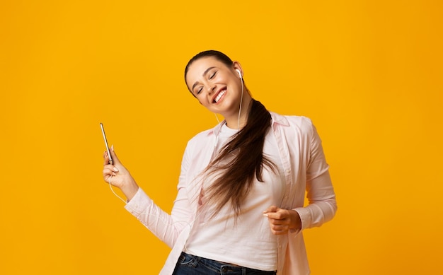 Alegre Dama Bailando Sosteniendo Smartphone Escuchando Música En Auriculares Fondo Amarillo