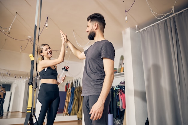 Alegre dama caucásica atlética saludando a su instructor de fitness con un máximo de cinco en un gimnasio