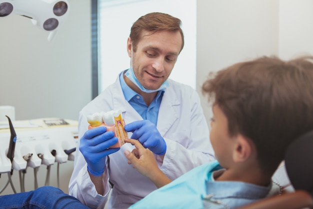 Alegre dentista masculino educar al niño sobre higiene dental