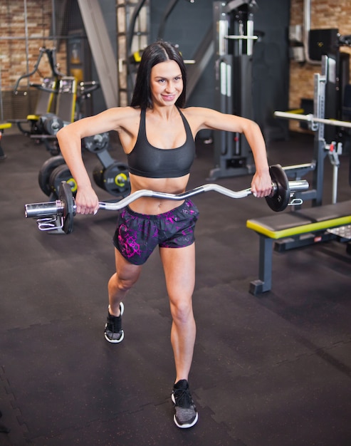 Alegre deportista morena decidida haciendo ejercicio con barra en las manos del gimnasio