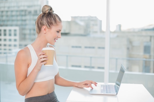 Alegre deportivo rubia usando laptop con café