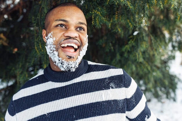 Alegre y divertido hombre africano con nieve en la barba disfrutando del clima invernal