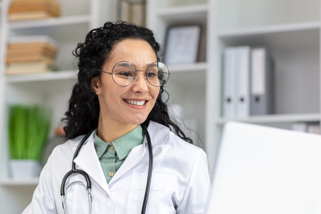 Una alegre doctora latina con gafas sonríe alegremente en el trabajo irradiando positividad y confianza