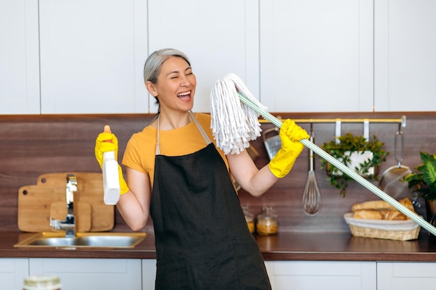 Alegre dona de casa asiática avental luvas dança esfregão de cozinha detergente